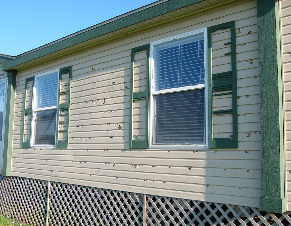 White home with hail damage on the siding and green trim